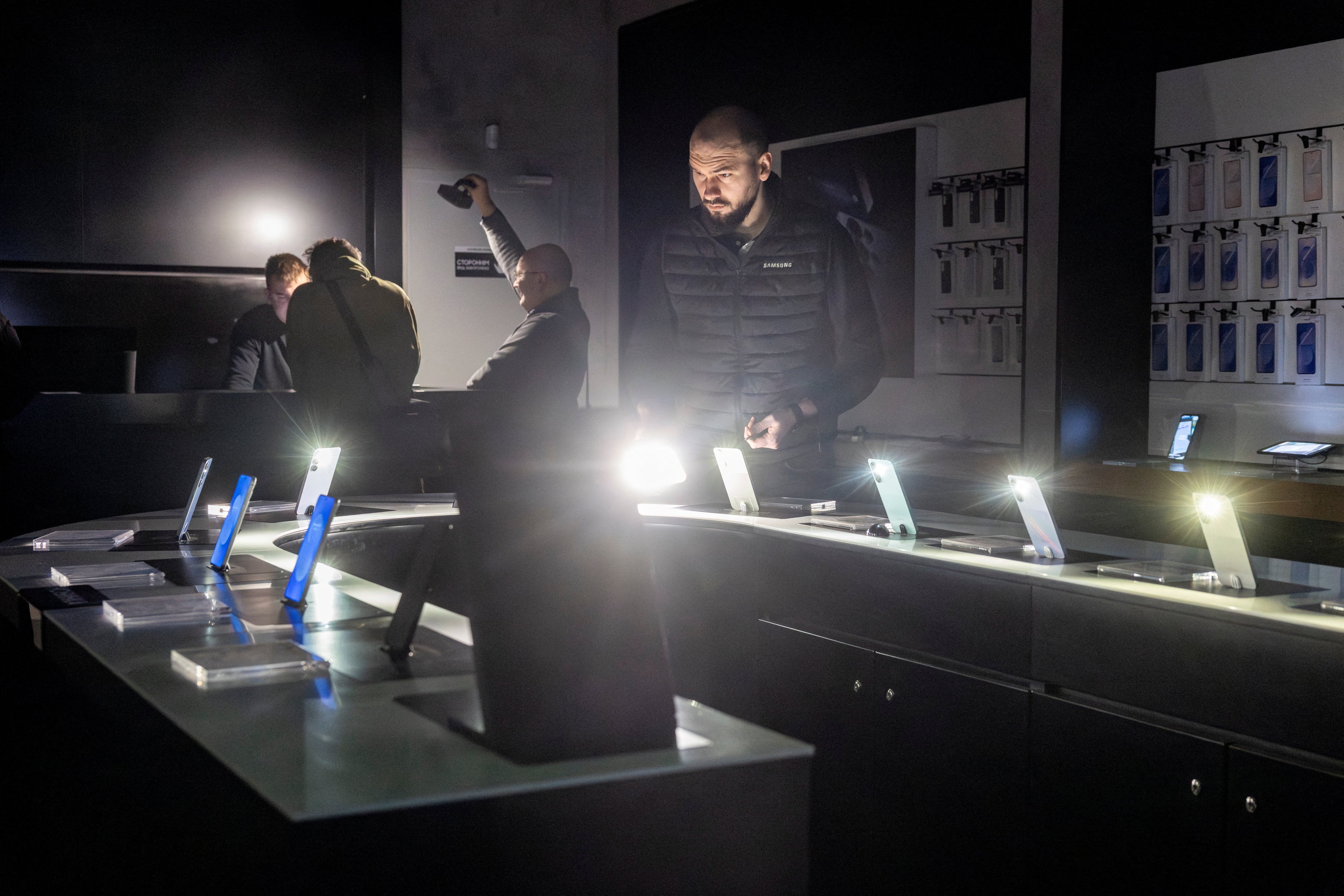 Un dependiente enciende las linternas de sus teléfonos inteligentes en una tienda de teléfonos móviles durante un apagón tras los recientes ataques rusos a la infraestructura civil de Ucrania, en medio del ataque de Rusia a Ucrania, en Járkov, Ucrania, el 31 de enero de 2026. REUTERS/Thomas Peter