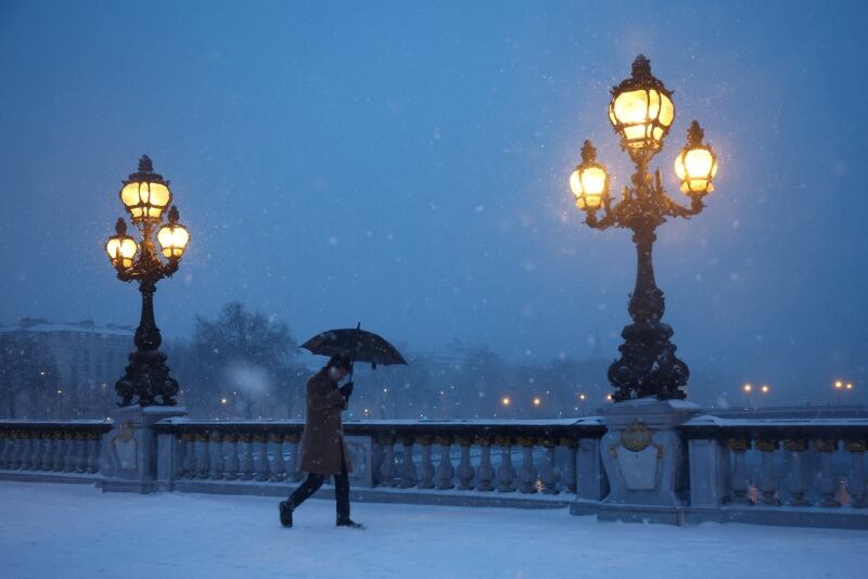 Un hombre se protege de la nieve que cae bajo un paraguas mientras camina por el Puente Alexandre III cubierto de nieve en París mientras el clima invernal con nieve y temperaturas frías azota una parte del país, Francia. 7 de enero de 2026 (REUTERS/Sarah Meyssonnier)