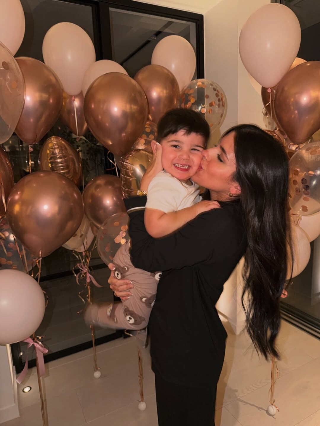 Valen sonríe mientras besa a su hijo pequeño, que ríe con deleite, rodeados de globos de colores rosados y dorados que celebran un momento especial (Instagram: valucervantes)