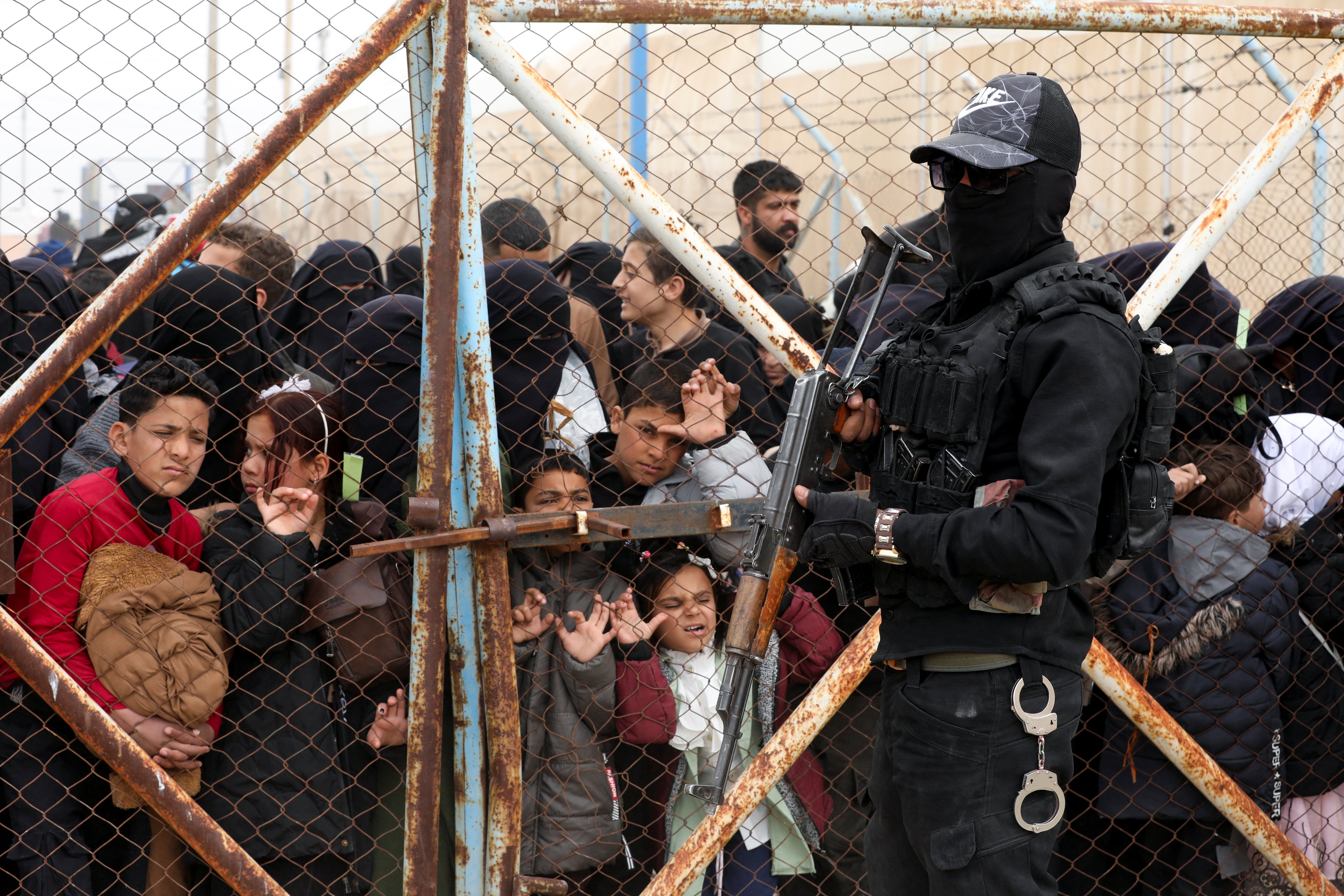 Un miembro de las Fuerzas Democráticas Sirias hace guardia junto a niños que miran a través de una valla anticiclón mientras las familias iraquíes en el campamento de Al-Hol se preparan para su viaje de regreso a Irak, en Siria, el 29 de marzo de 2025. REUTERS/Orhan Qereman