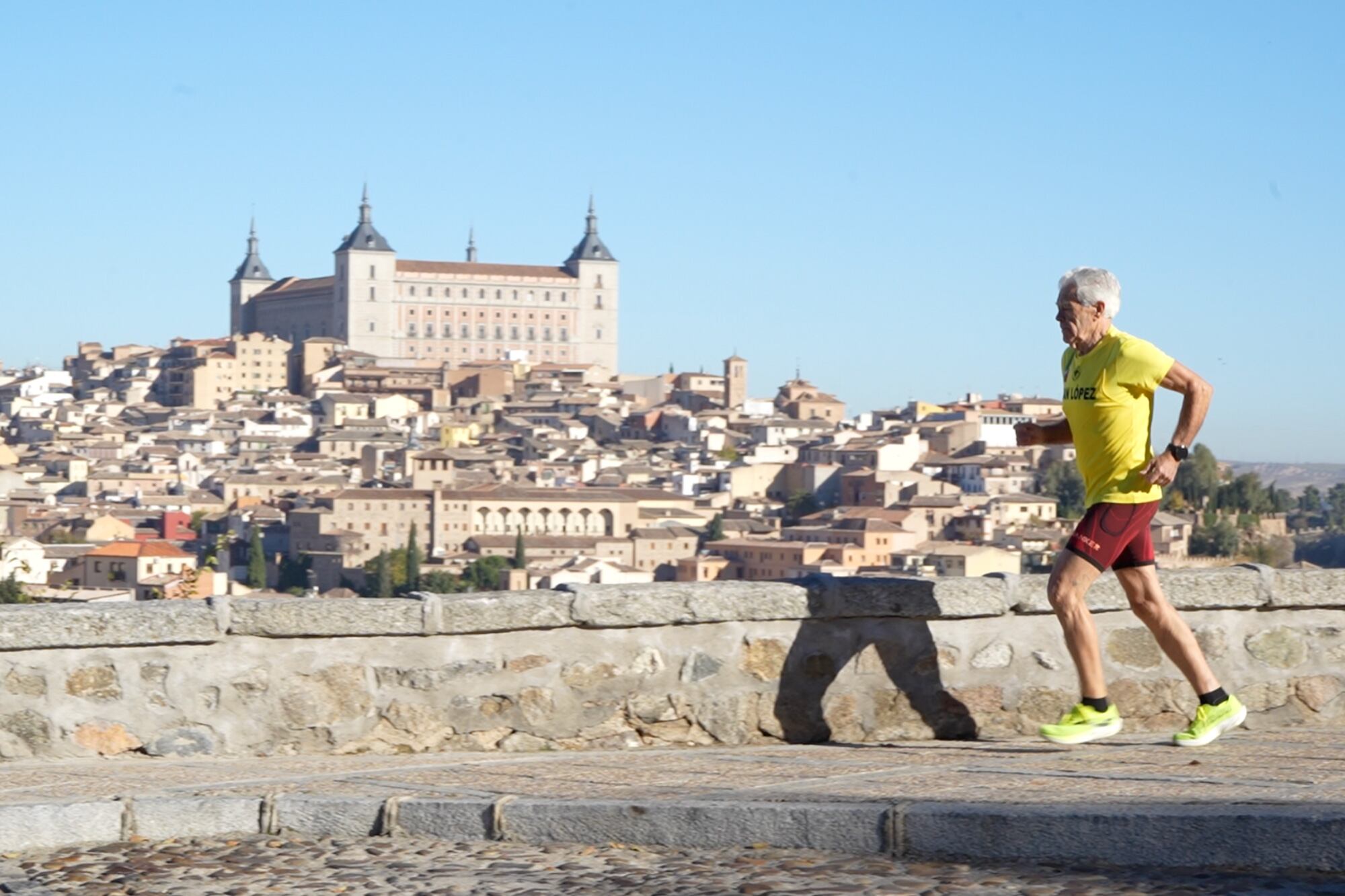 Juan López García, ultramaratonista de 82 años, corre por un camino empedrado con el histórico Alcázar de Toledo y la ciudad al fondo, demostrando su increíble vitalidad (The Washington Post)