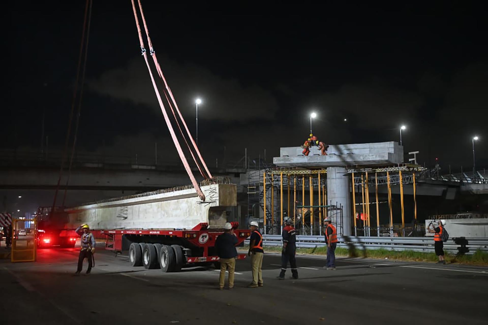 Trabajadores de la construcción transportan e instalan una viga prefabricada durante la noche como parte de los trabajos de ampliación y mejora del Puente Labruna.