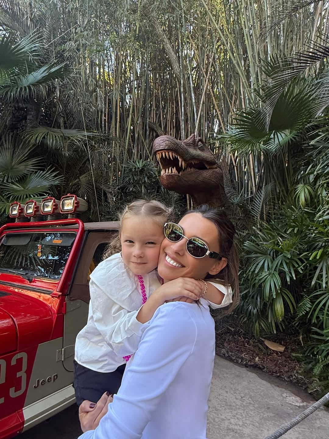 Pampita sonríe mientras abraza a su hija Anita García Moritán, posando junto a una figura de dinosaurio y un jeep en un parque temático de Universal en Estados Unidos.