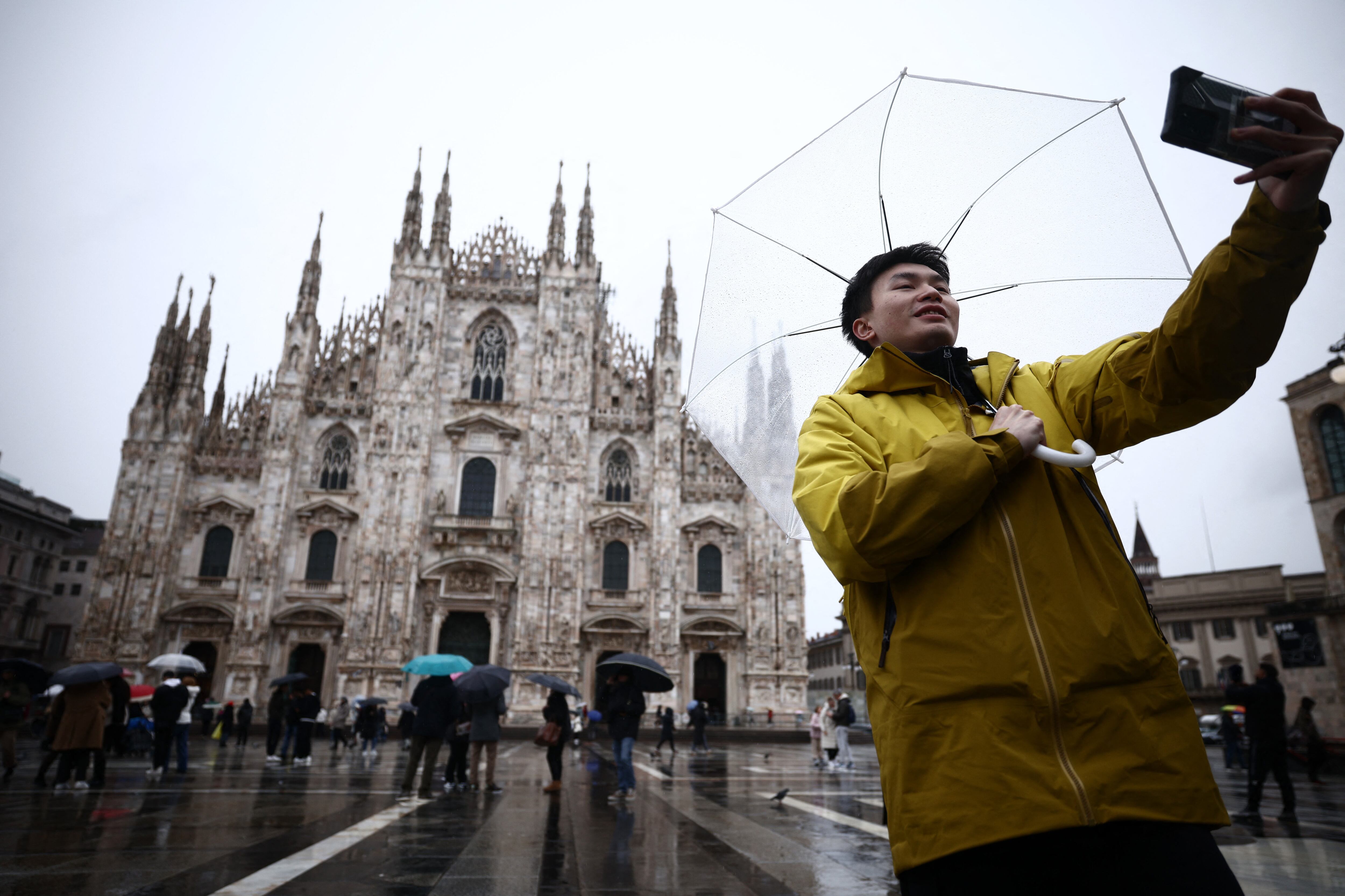 Milano Cortina 2026 Winter Olympics - Preview - Milan, Italy - February 4, 2026 A man holding an umbrella takes a selfie outside the Duomo di Milano