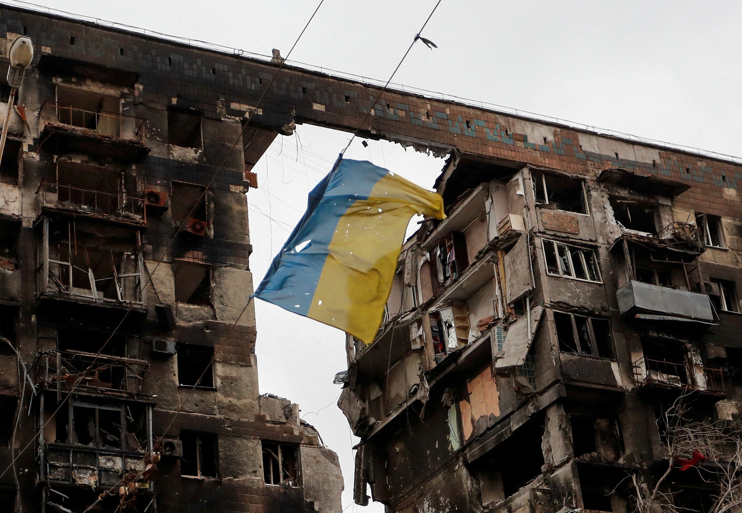 Una bandera ucraniana rota colgada de un alambre frente a un edificio de apartamentos destruido durante el conflicto entre Ucrania y Rusia en la ciudad portuaria de Mariupol, en el sur de Ucrania, el 14 de abril de 2022 (REUTERS/Alexander Ermochenko)