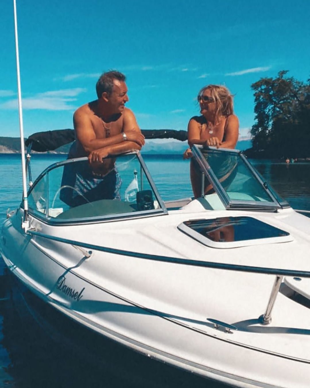 Chino Tapia y Viviana Juricka sonríen mientras disfrutan de un relajante día a bordo de un bote en un lago de aguas tranquilas bajo un cielo despejado.