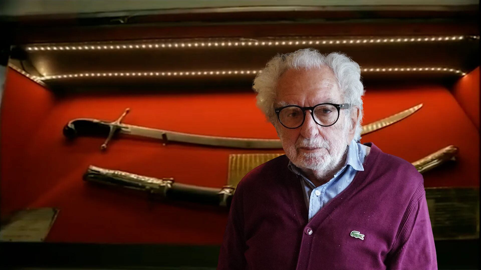 El historiador Pacho O'Donnell posa frente al Sable Corvo del General San Martín, exhibido en una vitrina iluminada, un símbolo crucial de la independencia argentina (Imagen Ilustrativa Infobae)