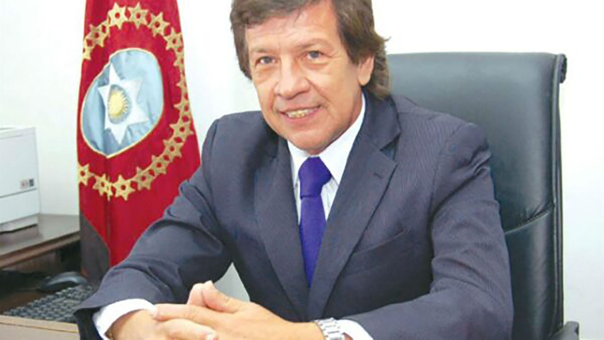 El ex fiscal federal de Orán, José Luis Bruno, sonríe mientras está sentado en su oficina, con una bandera institucional de fondo.