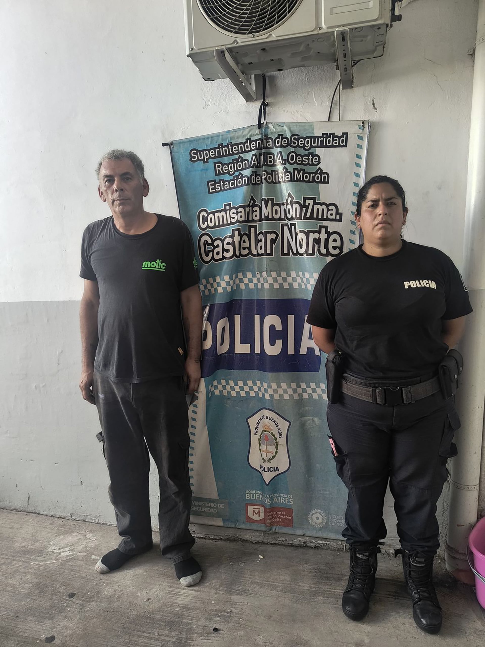 El agresor cuando fue detenido junto a una oficial de la Policía Bonaerense frente a un banner de la Comisaría Morón 7ma. Castelar Norte