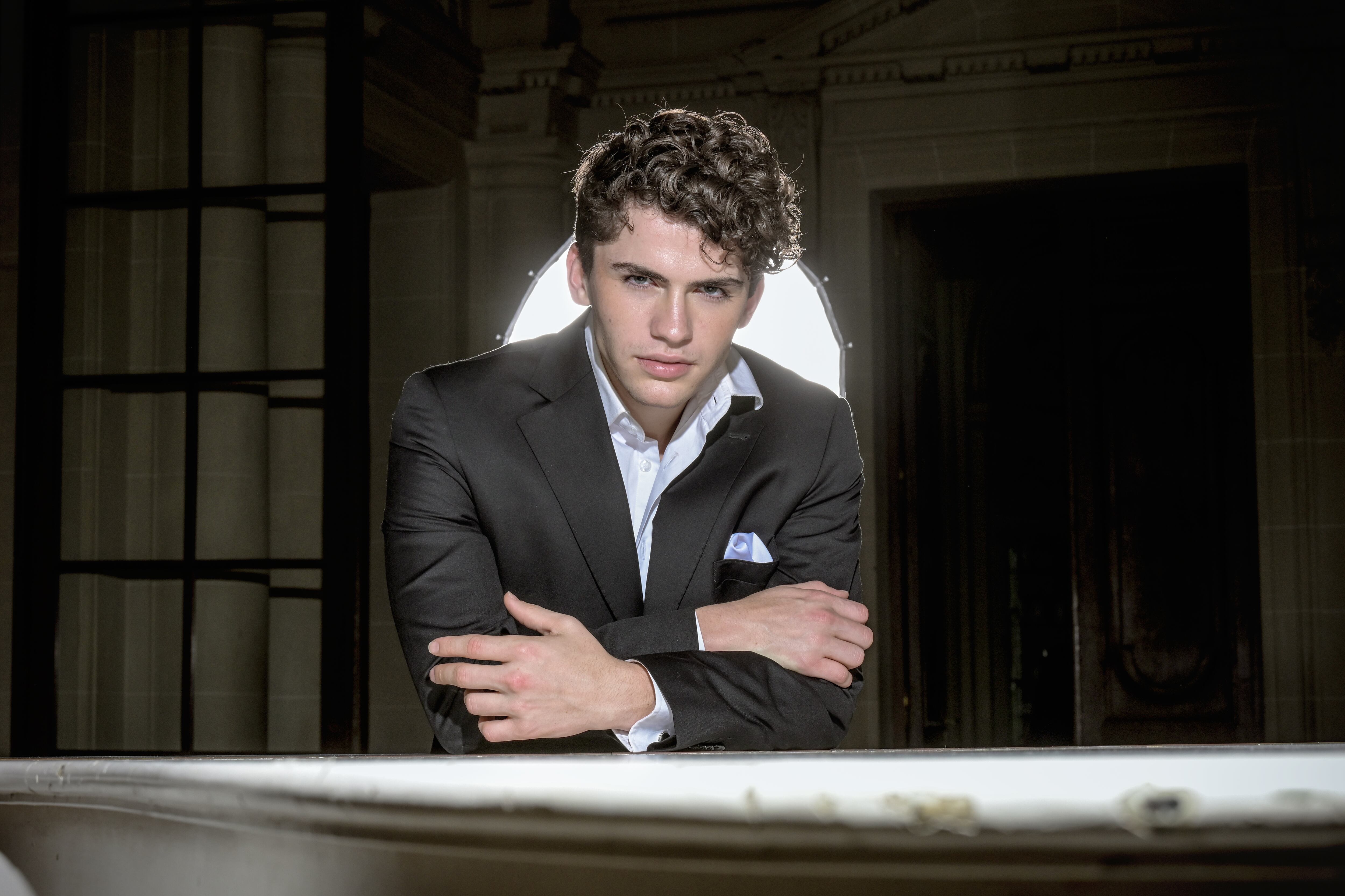 El cantante Martín Savi posa para un retrato oficial, luciendo un elegante traje negro con una camisa blanca y un pañuelo de bolsillo azul claro, con una fuerte luz de fondo. (Federico de Bartolo)