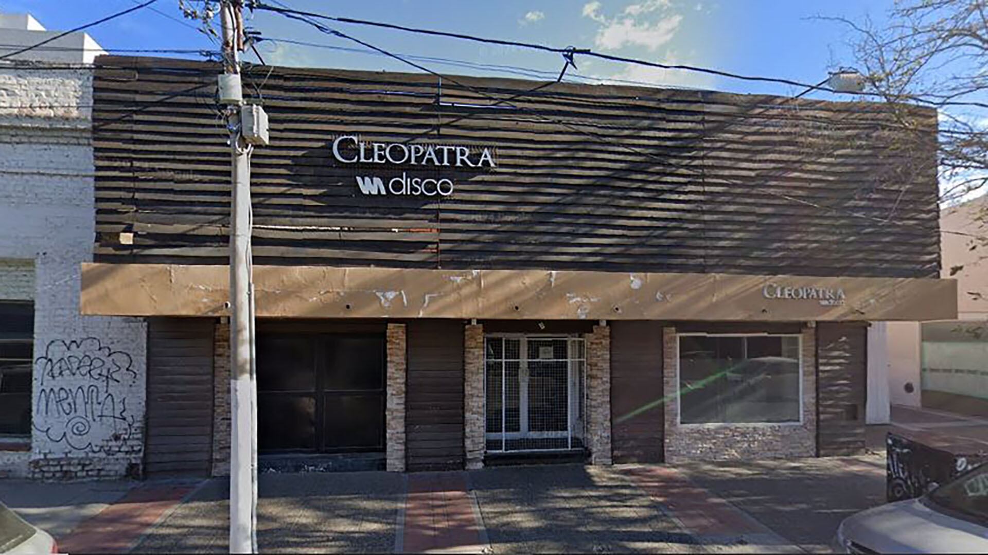 Vista frontal del edificio comercial que albergaba el local nocturno Cleopatra Disco, con su fachada marrón y beige, enmarcado por un poste de servicios públicos en una calle urbana.