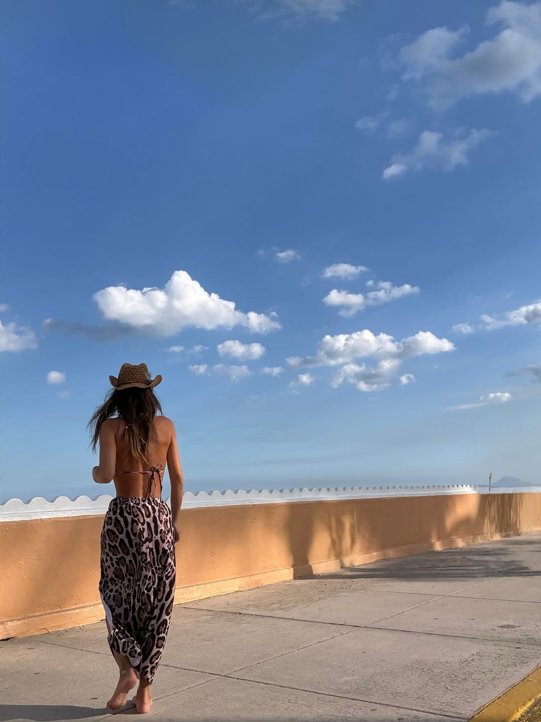 Pampita camina descalza por un paseo marítimo bajo el cielo azul