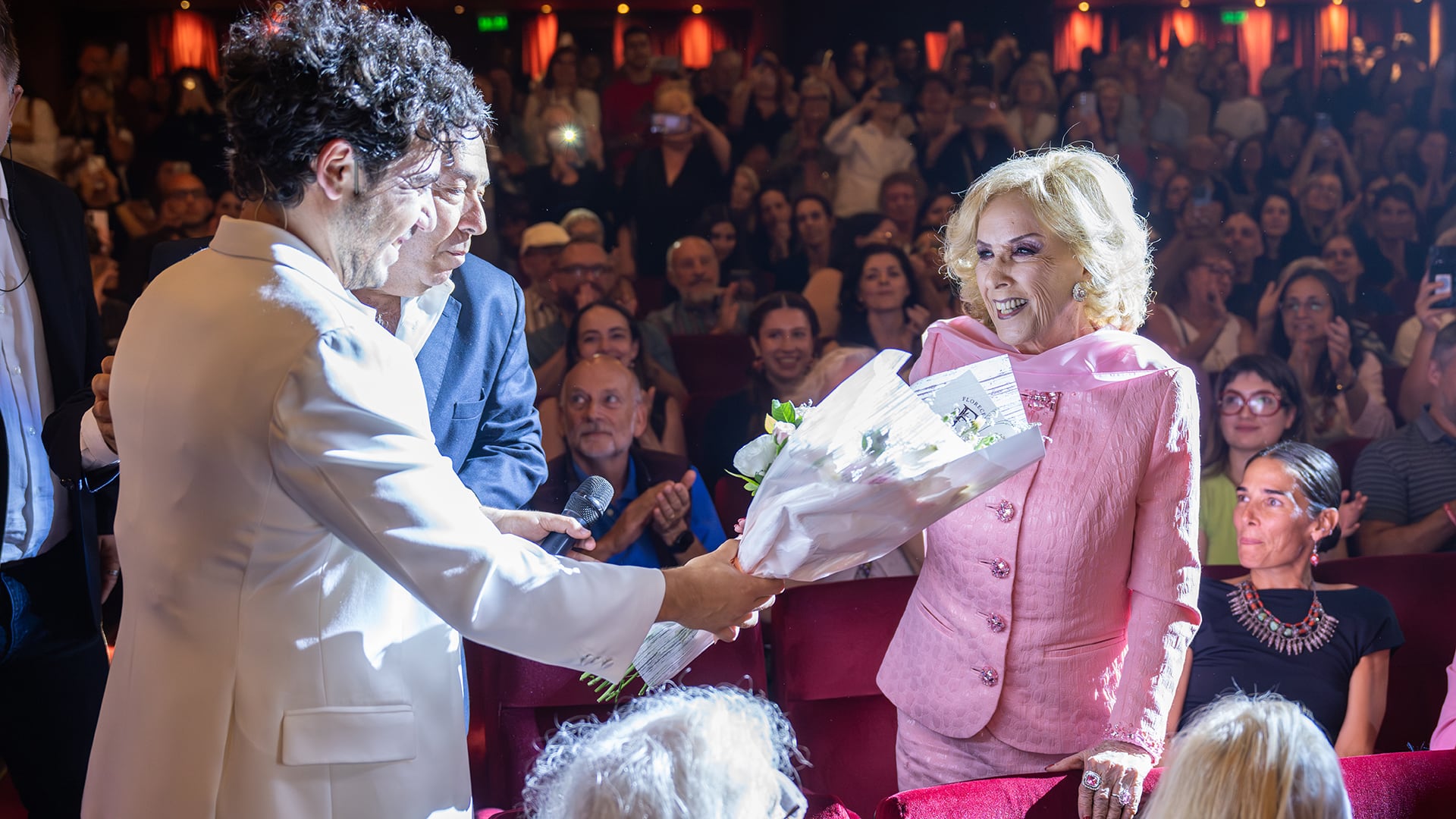 Mirtha Legrand, vestida de rosa y con una sonrisa radiante, recibe un ramo de flores de manos de Fer Dente, acompañada por Juana Viale y el aplauso del público tras la función de 