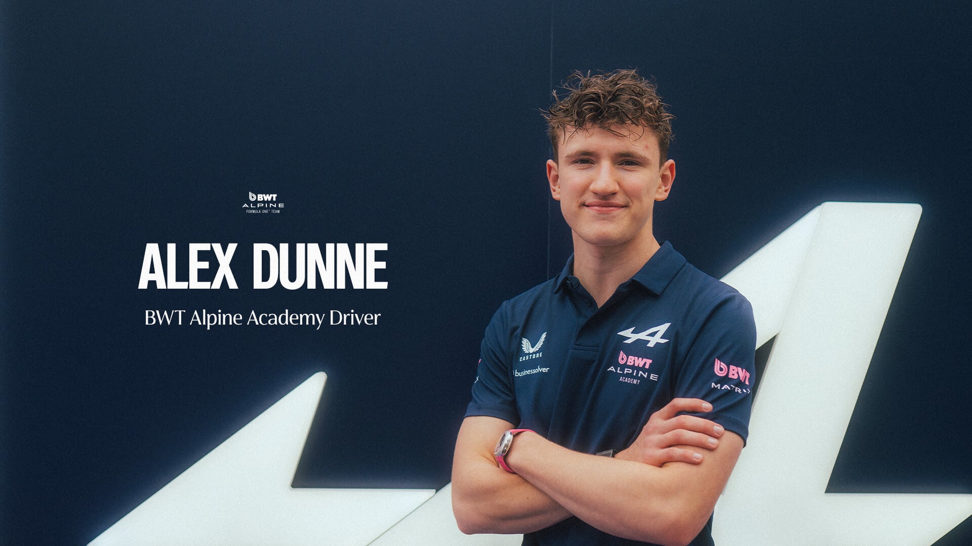 Alex Dunne, piloto de la Academia BWT Alpine, posa con los brazos cruzados frente a un fondo oscuro con el logotipo de su equipo.