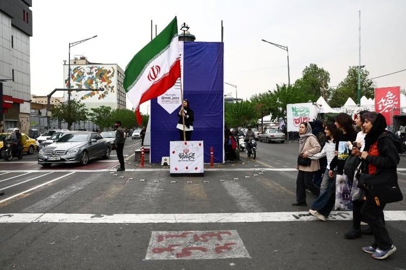 Una mujer sostiene una bandera iraní en una calle, en medio de un alto el fuego entre Estados Unidos e Irán, en Teherán, Irán. 20 de abril de 2026 (ERUTERS)