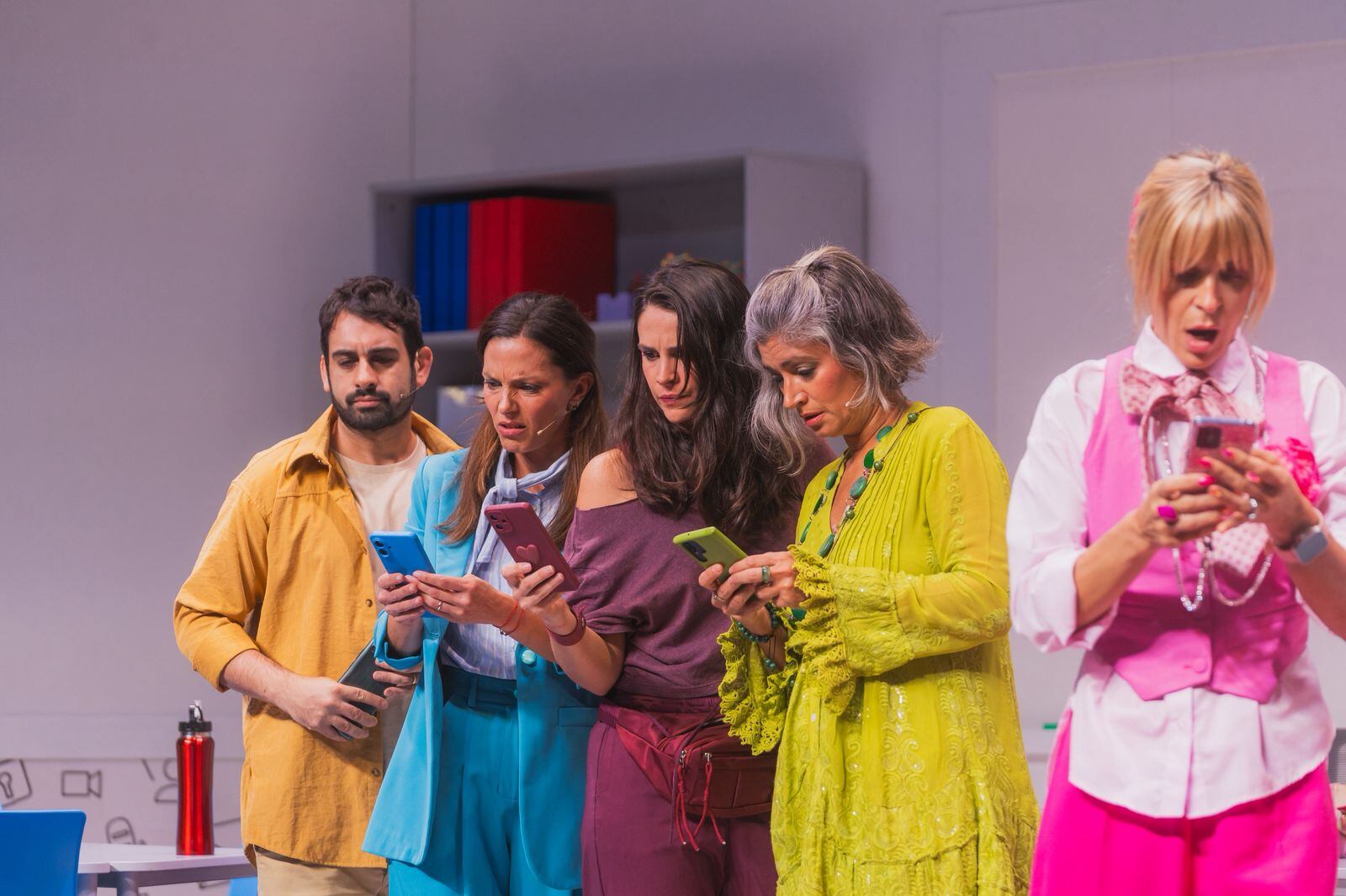Lionel Arostegui, Manuela Pal, Mica Riera, Carla Conte y Eugenia Tobal concentrados en sus teléfonos celulares durante una representación teatral, reflejando la omnipresencia de la tecnología.