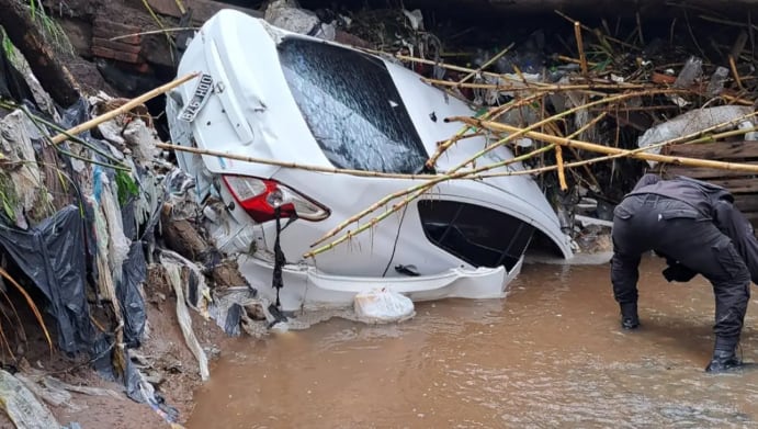 Un vehículo blanco volcado y rodeado de escombros es inspeccionado en un canal de Tucumán, donde una pareja falleció tras quedar atrapada por la crecida
