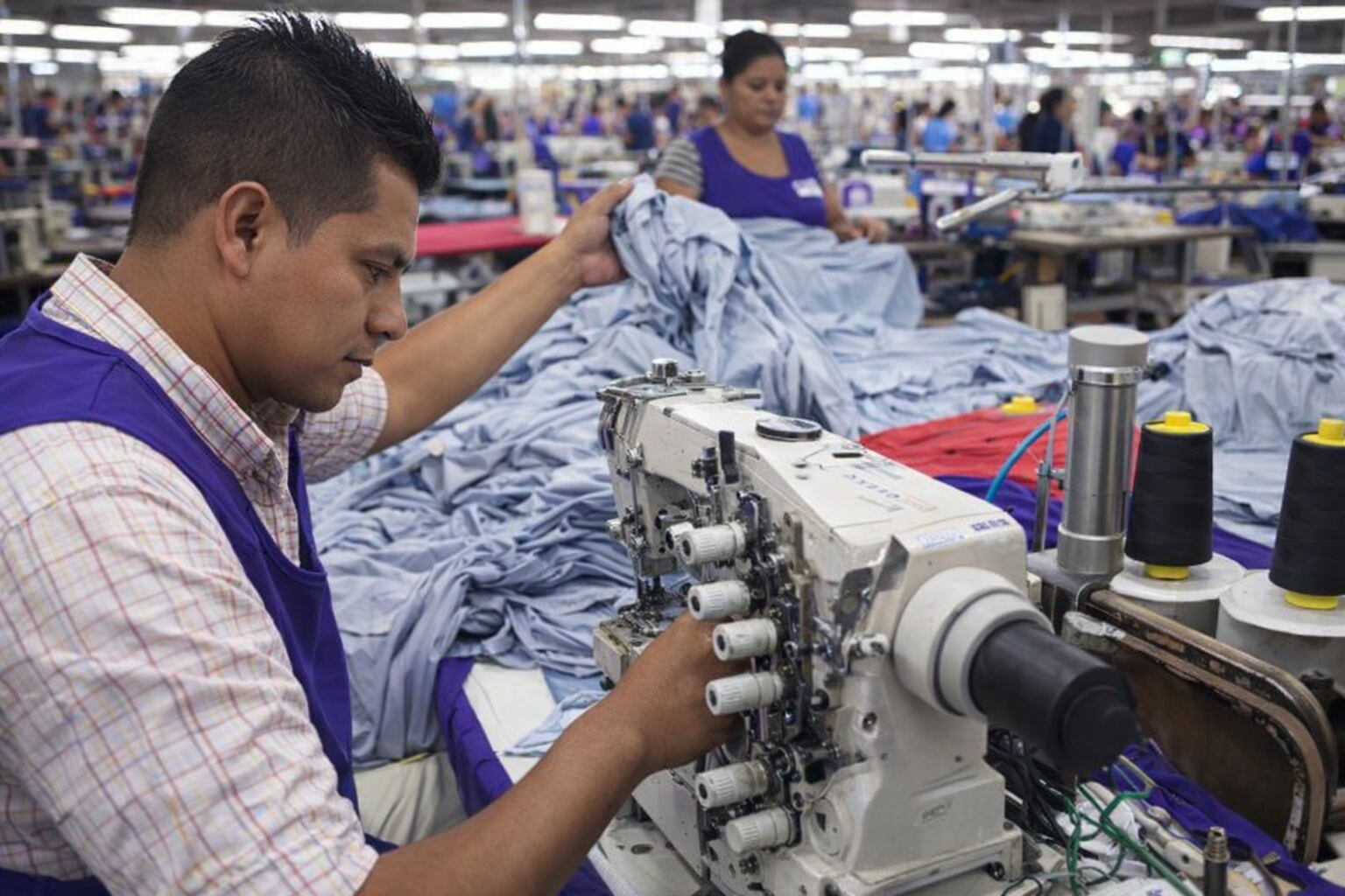 Un operario de la maquila textil en El Salvador trabaja con destreza en una máquina de coser, contribuyendo a la producción de prendas de vestir en una fábrica concurrida. (Imagen Ilustrativa Infobae)