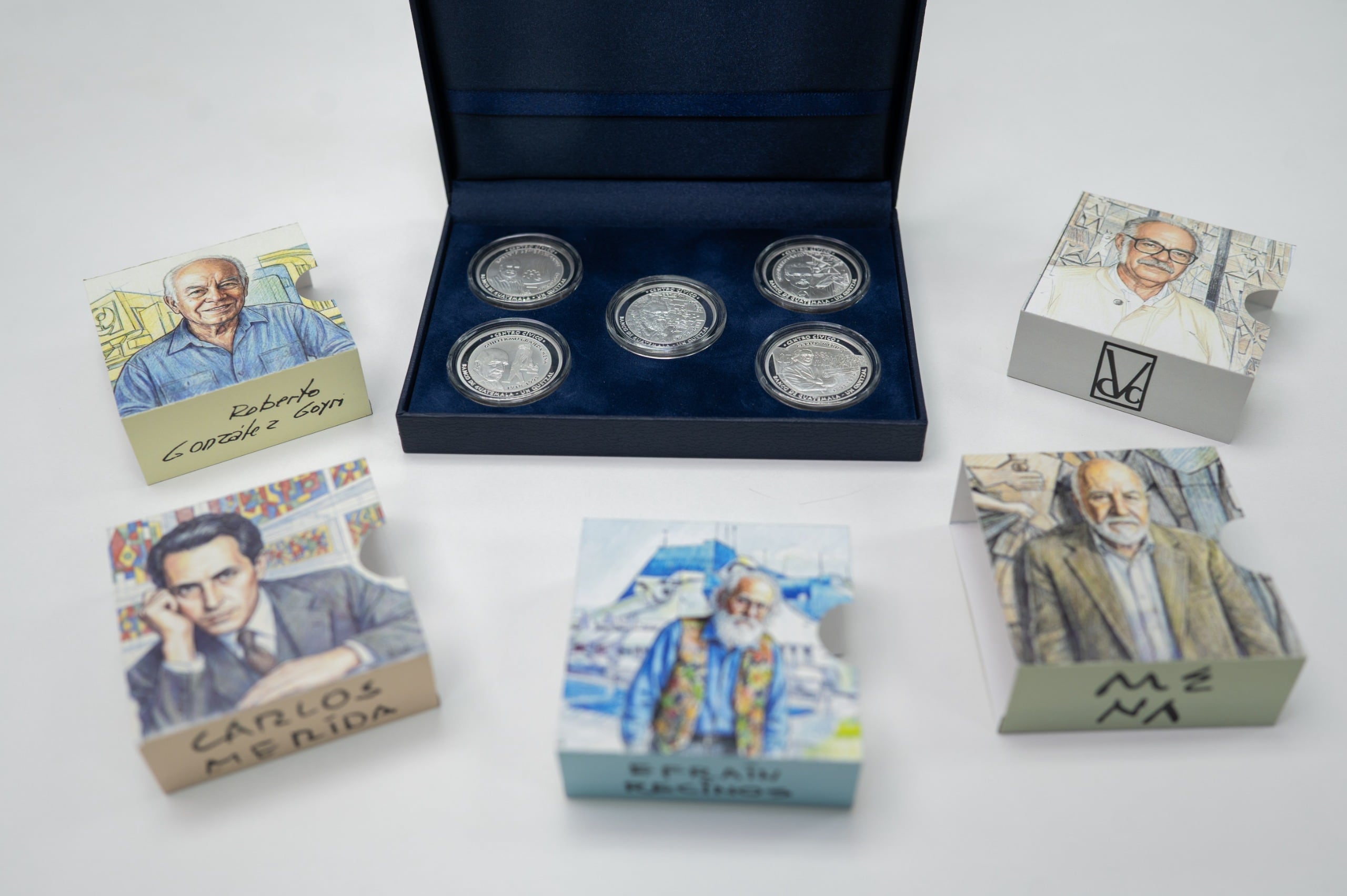 Un conjunto de monedas conmemorativas del Banco de Guatemala, que rinden homenaje a destacados artistas y arquitectos guatemaltecos relacionados con el Centro Cívico, se exhibe junto a retratos ilustrados. (Banco de Guatemala)