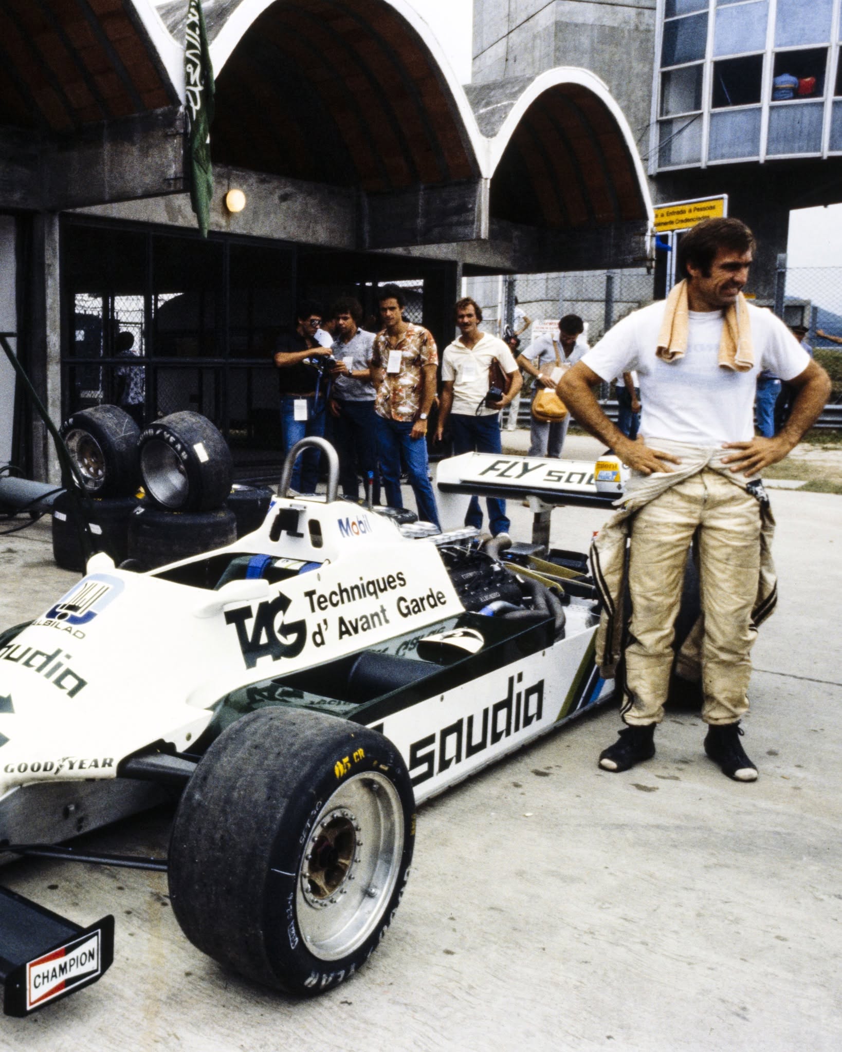 Carlos Reutemann, piloto de Fórmula 1, se muestra relajado junto a su monoplaza blanco con patrocinio Saudia en el área de boxes.