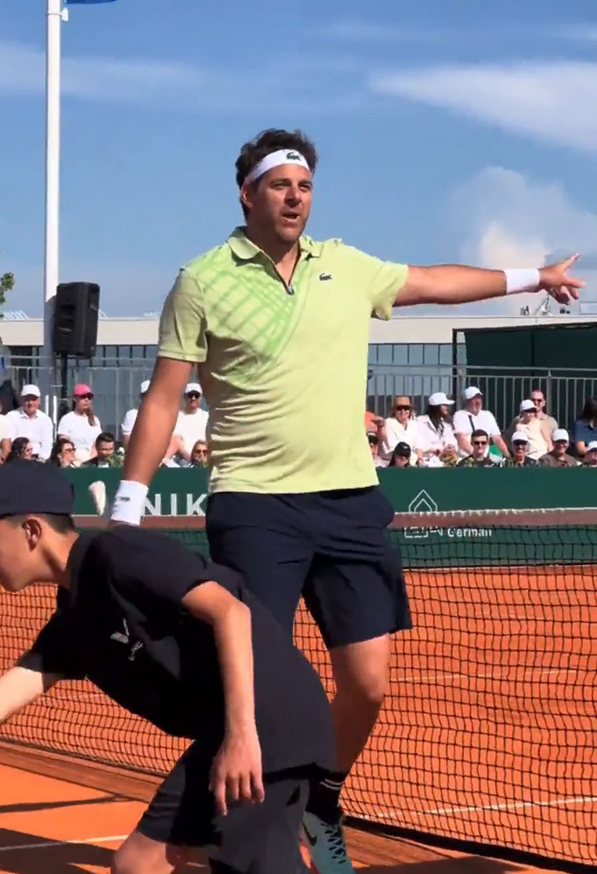 Juan Martín del Potro interactúa con el público mientras participa en una exhibición de tenis en una cancha de arcilla bajo un cielo despejado.