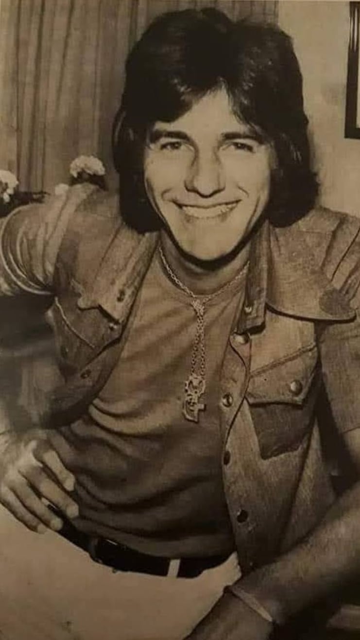 Un joven Sergio Denis posa sonriente para un retrato en blanco y negro con un look típico de los años '70