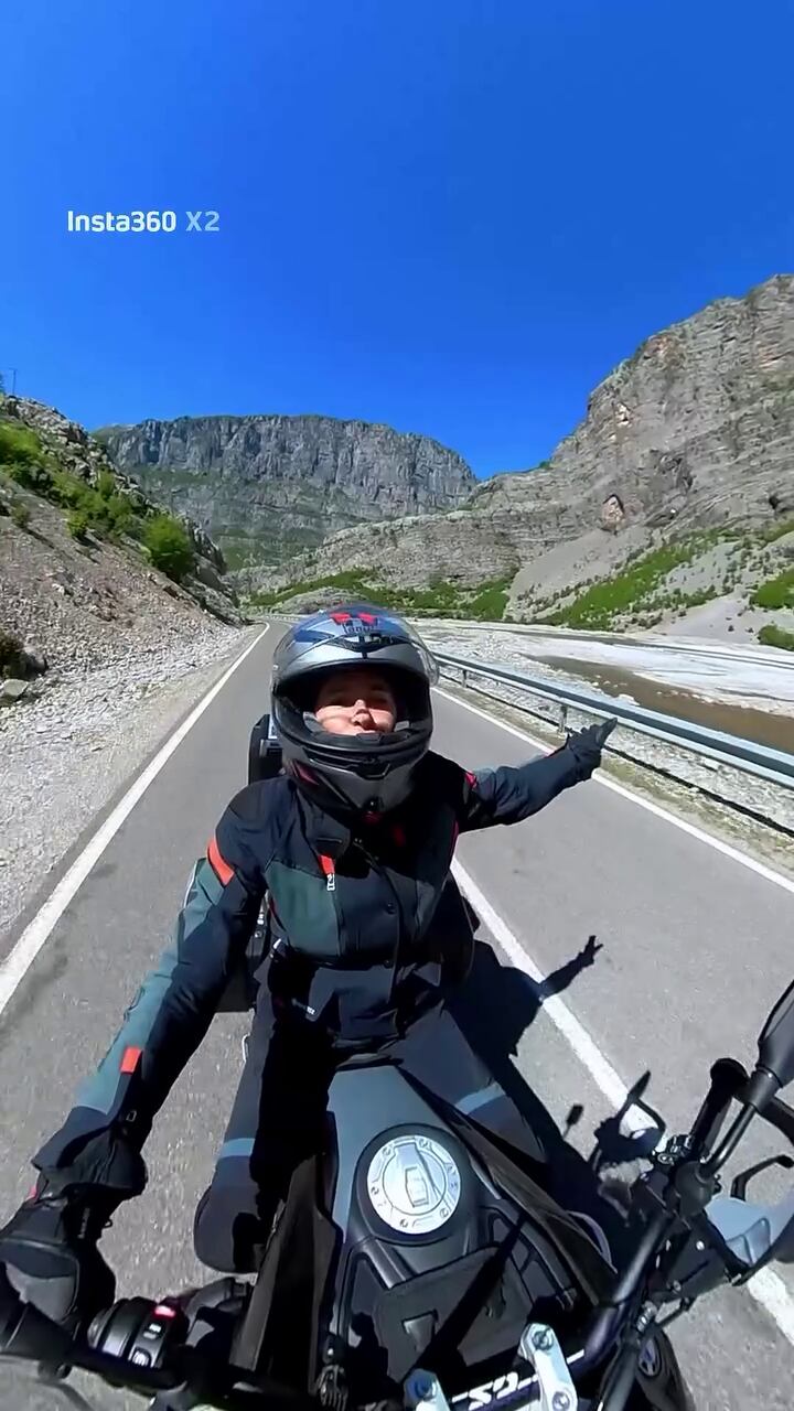 Carolina Baldini sonríe y señala mientras conduce su moto por una carretera montañosa, parte de su viaje de Croacia a Grecia, un símbolo de libertad y nuevos inicios.