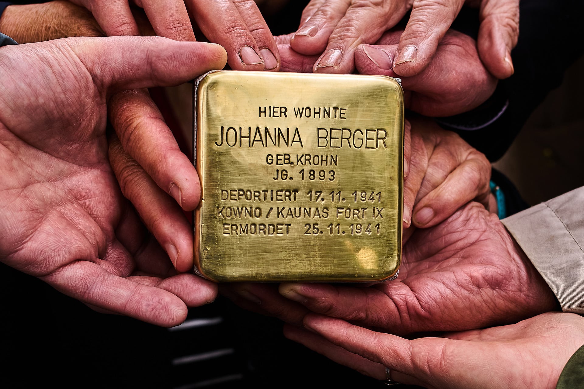 Varias manos sostienen un Stolperstein de latón, un monumento a Johanna Berger que conmemora su deportación y asesinato durante el Holocausto. (AP)