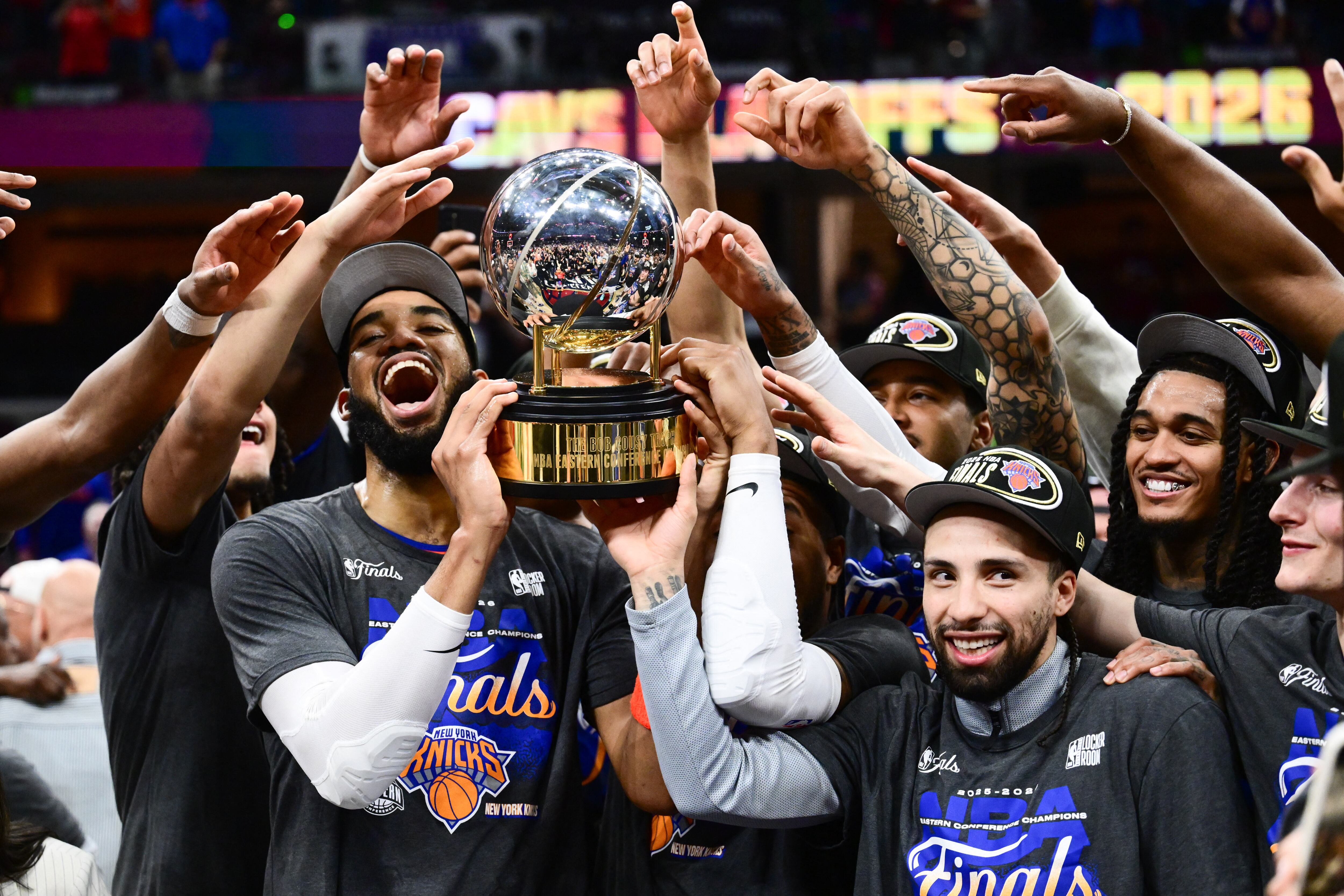 El pívot de los New York Knicks, Karl-Anthony Towns (32) y el base José Alvarado (5), ayudan al equipo a levantar el trofeo tras derrotar a los Cleveland Cavaliers en el cuarto juego de las finales de la Conferencia Este para los playoffs de la NBA de 2026 en Rocket Arena (Crédito obligatorio: Ken Blaze-Imagn Images)