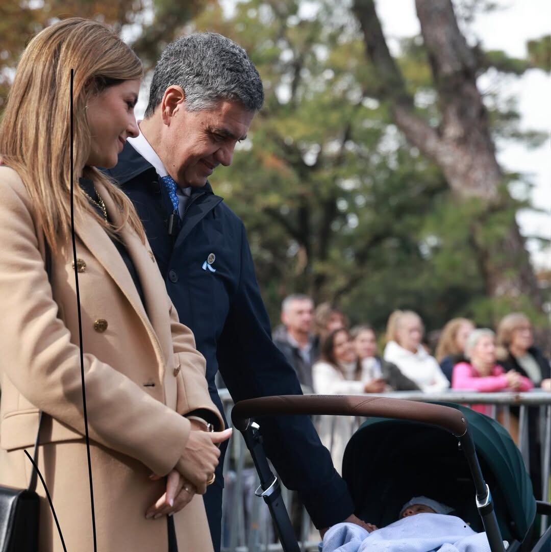 María Belén Ludueña y Jorge Macri junto a su hijo Vito, mirándolo en su cochecito durante un evento al aire libre (Instagram)