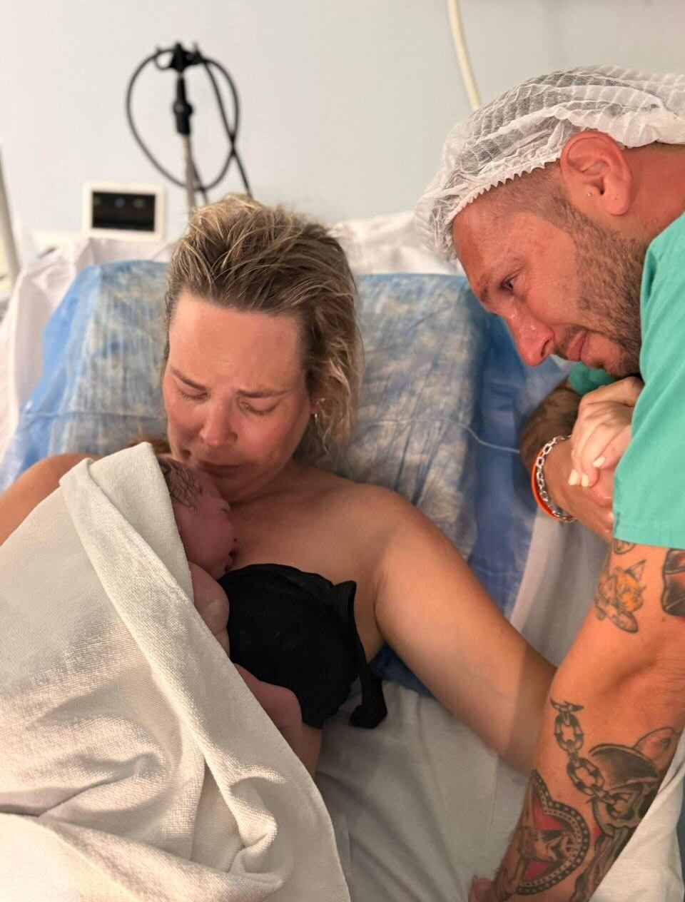 Muni, visiblemente emocionada, sosteniendo a su recién nacido Vicente mientras su pareja observa con lágrimas en los ojos en la sala de partos