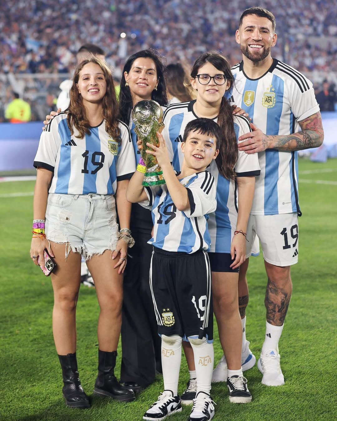 El futbolista Nicolás Otamendi y su pareja Celeste Rey posan felices con sus hijos y la Copa del Mundo en el campo de juego.