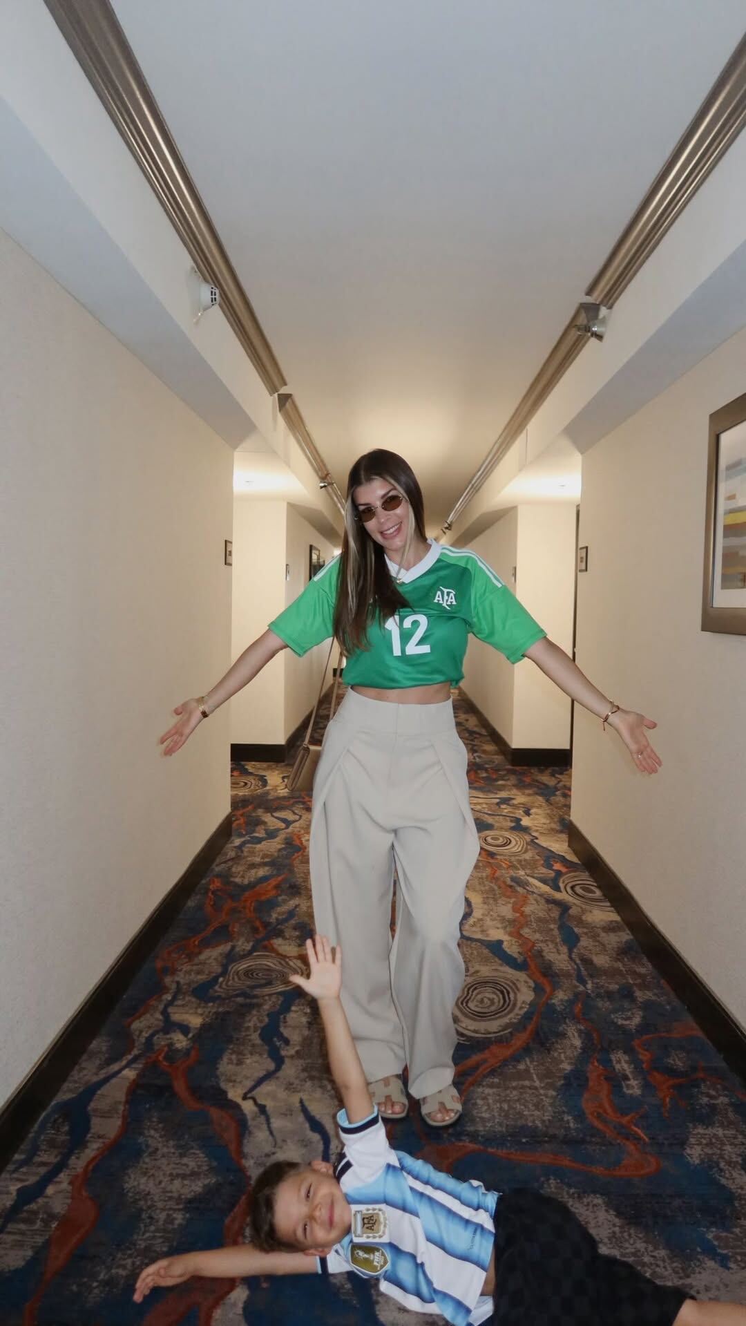 Rocío Espósito sonríe en un pasillo de hotel con una camiseta de fútbol, acompañada por el hijo de Gerónimo Rulli, quien viste la de Argentina.