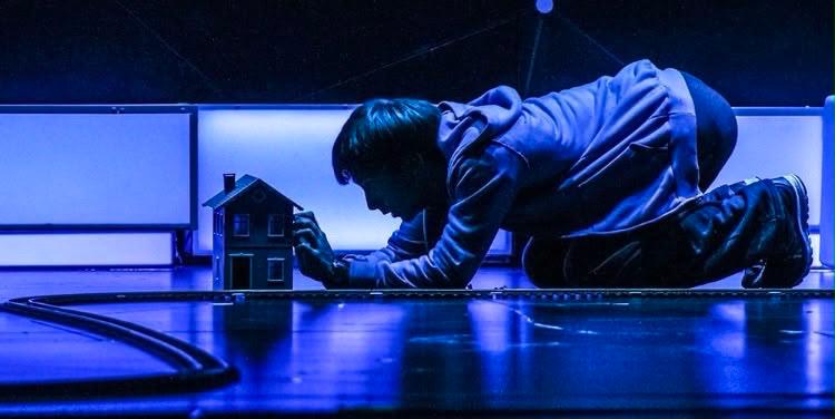Iñaki Aldao se arrodilla ante una casa en miniatura y una vía de tren, reflejando la complejidad del mundo de Christopher Boone en la aclamada obra de teatro 'El curioso incidente del perro a medianoche' (Gentileza de Prensa)