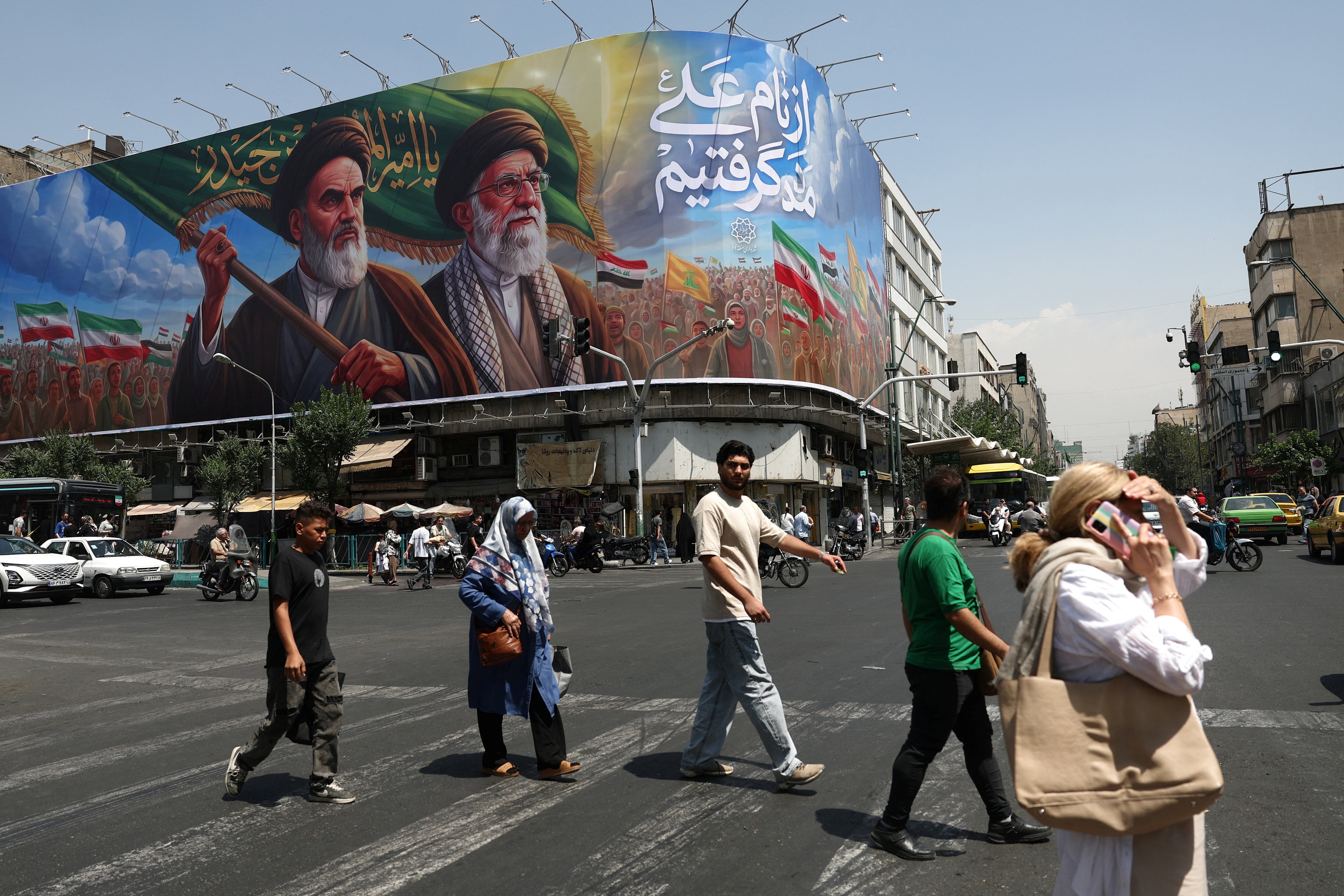 La gente pasa junto a una valla publicitaria en la que aparecen el difunto líder de la Revolución Islámica, el ayatollah Ruhollah Jomeini, y el difunto líder supremo de Irán, el ayatollah Alí Khamenei, en una calle de Teherán (REUTERS)