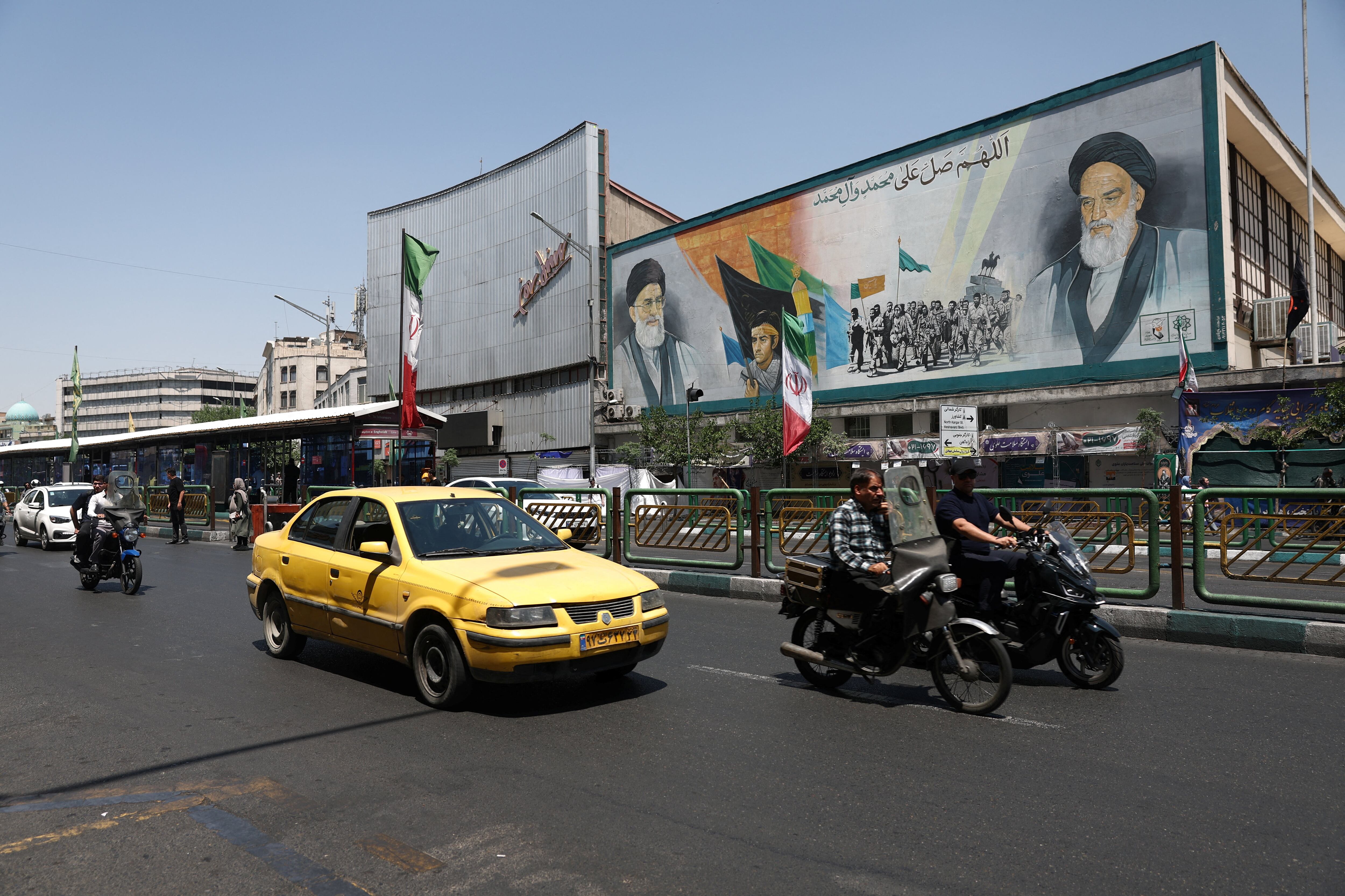 Varias personas pasan en bicicleta junto a un mural que representa al difunto líder de la Revolución Islámica, el ayatolá Ruhollah Jomeini, y al difunto líder supremo de Irán, el ayatolá Ali Jamenei, en una calle de Teherán, Irán, el 9 de junio de 2026. Majid Asgaripour/WANA (Agencia de Noticias de Asia Occidental) vía REUTERS