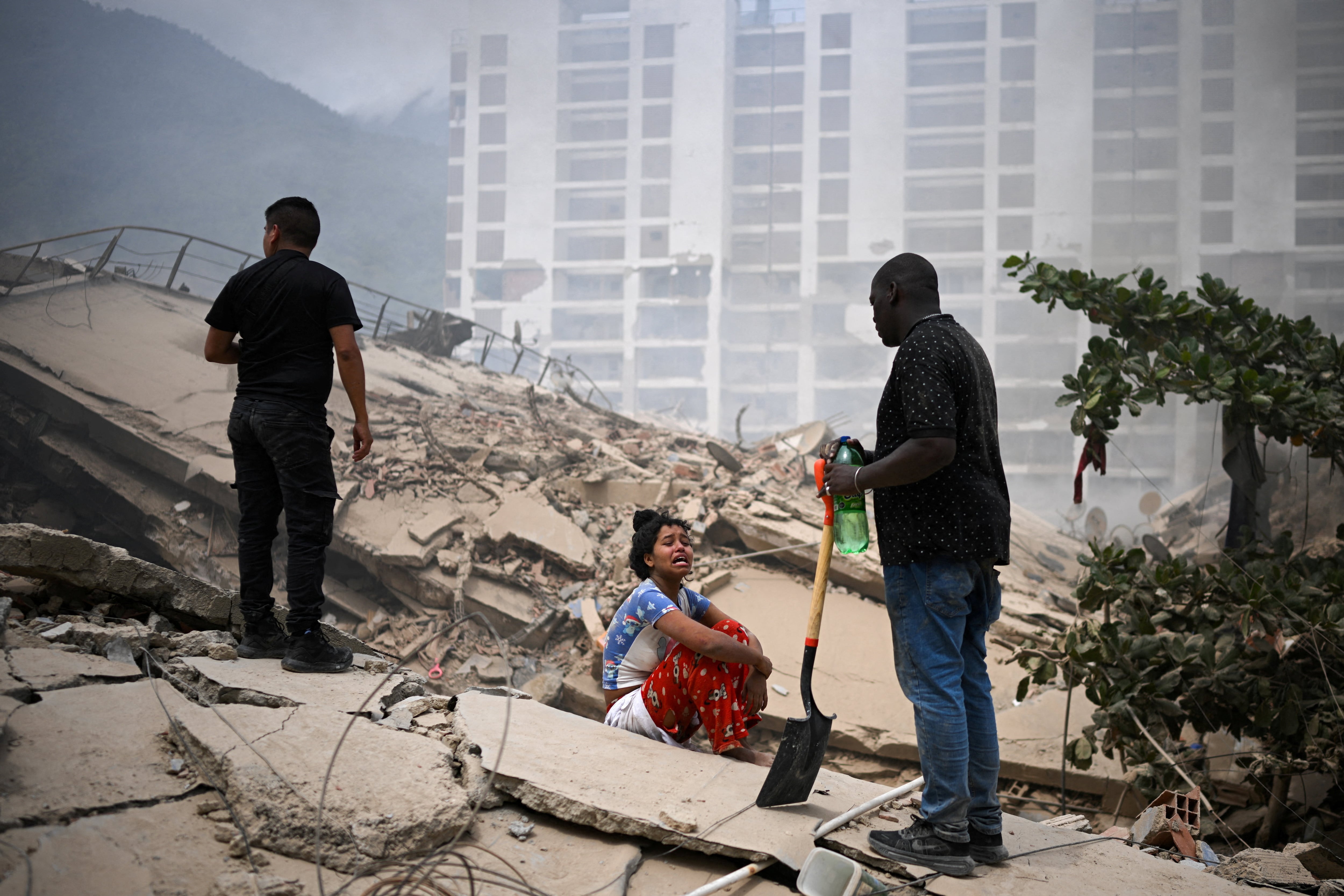 Rescatistas trabajan entre los restos de edificaciones derrumbadas mientras una mujer sigue de cerca la búsqueda de sobrevivientes en La Guaira (REUTERS)
