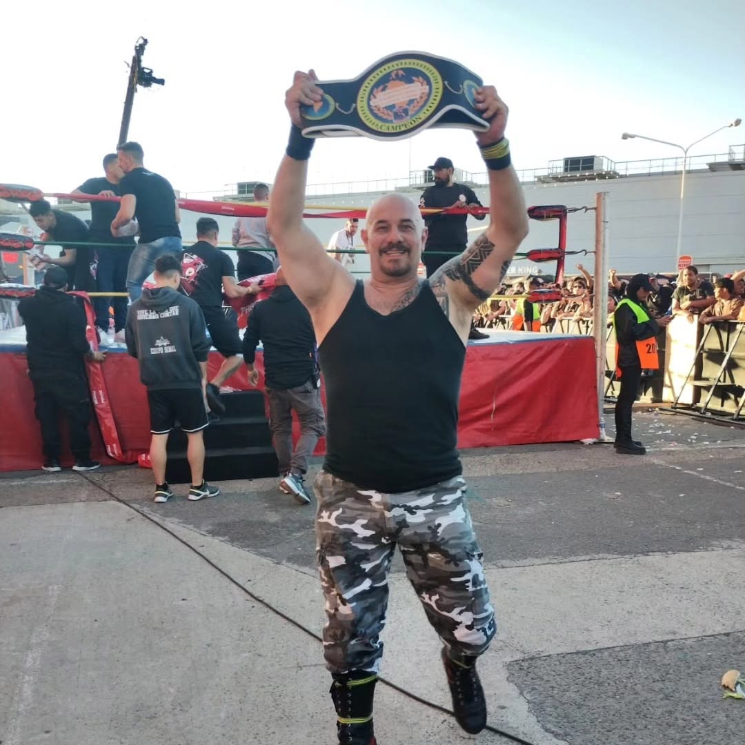 El luchador Pablo Más Albert, conocido como Teniente Murphy de 100% Lucha, sostiene el cinturón de campeón durante su despedida en un evento al aire libre.