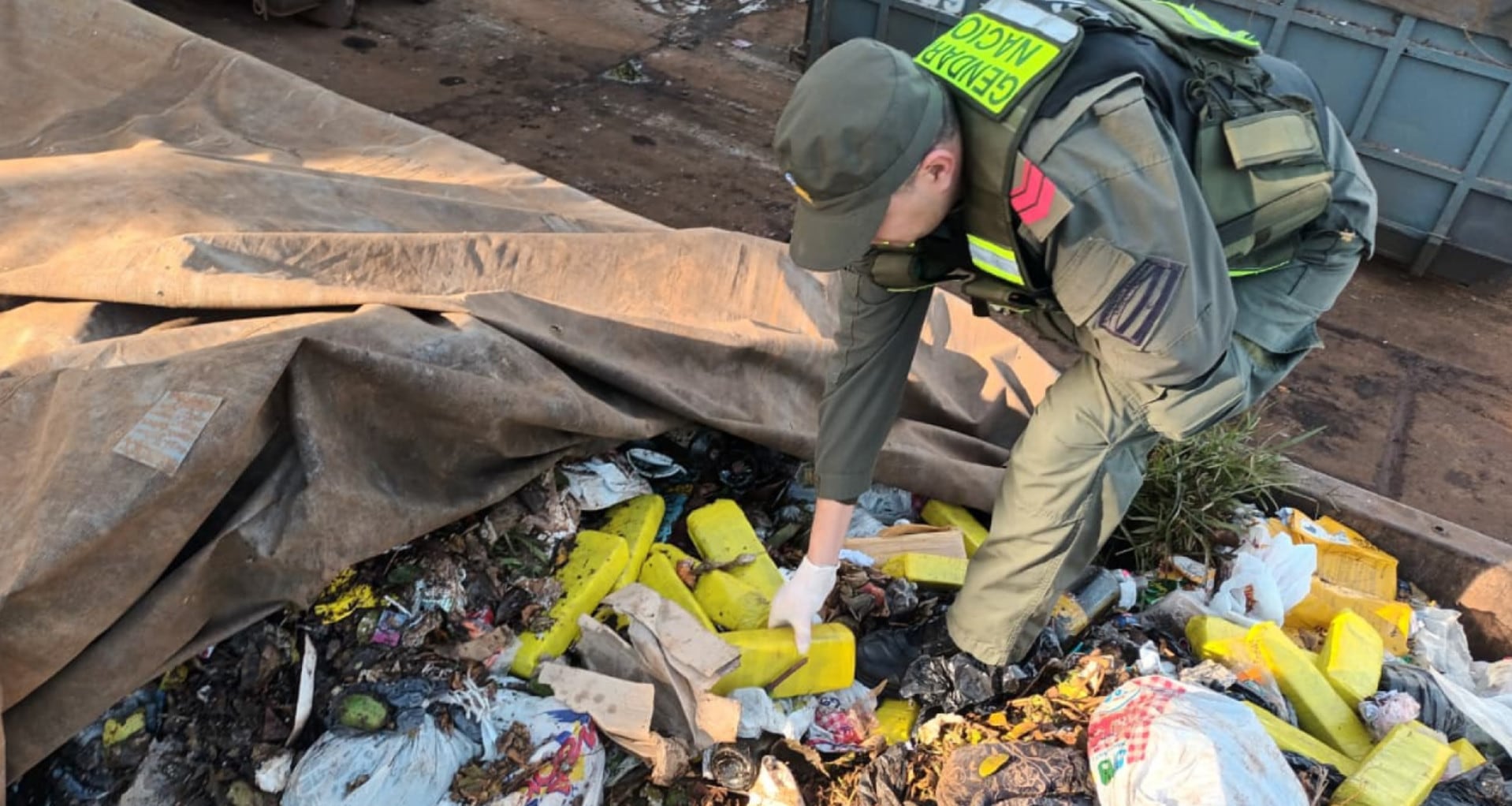 Un agente de Gendarmería Nacional inspecciona paquetes de marihuana descubiertos entre la basura de un contenedor en una planta de residuos en Posadas, Misiones (GNA)