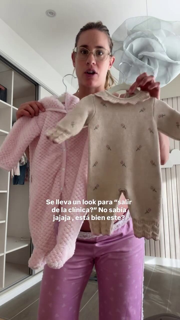 Julieta Puente sostiene dos prendas de bebé, un enterito rosa y otro tejido con patrones, mientras organiza los preparativos en su casa