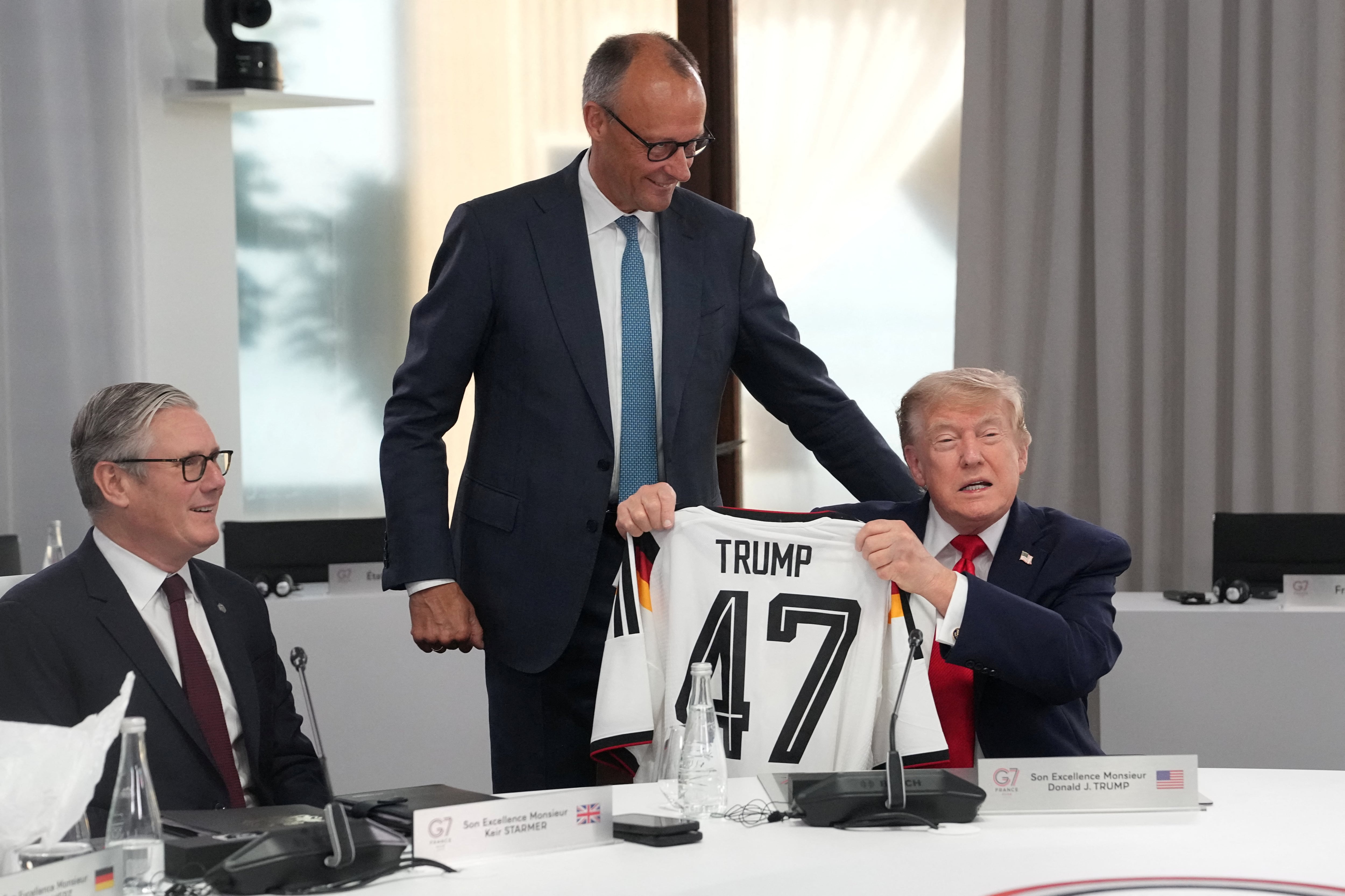El canciller alemán Friedrich Merz entrega al presidente estadounidense Donald Trump una camiseta con el número 47, mientras el primer ministro británico Keir Starmer observa, durante una sesión de trabajo en la cumbre del G7 en Evian-les-Bains, Francia, el 16 de junio de 2026. Thibault Camus/Pool vía REUTERS