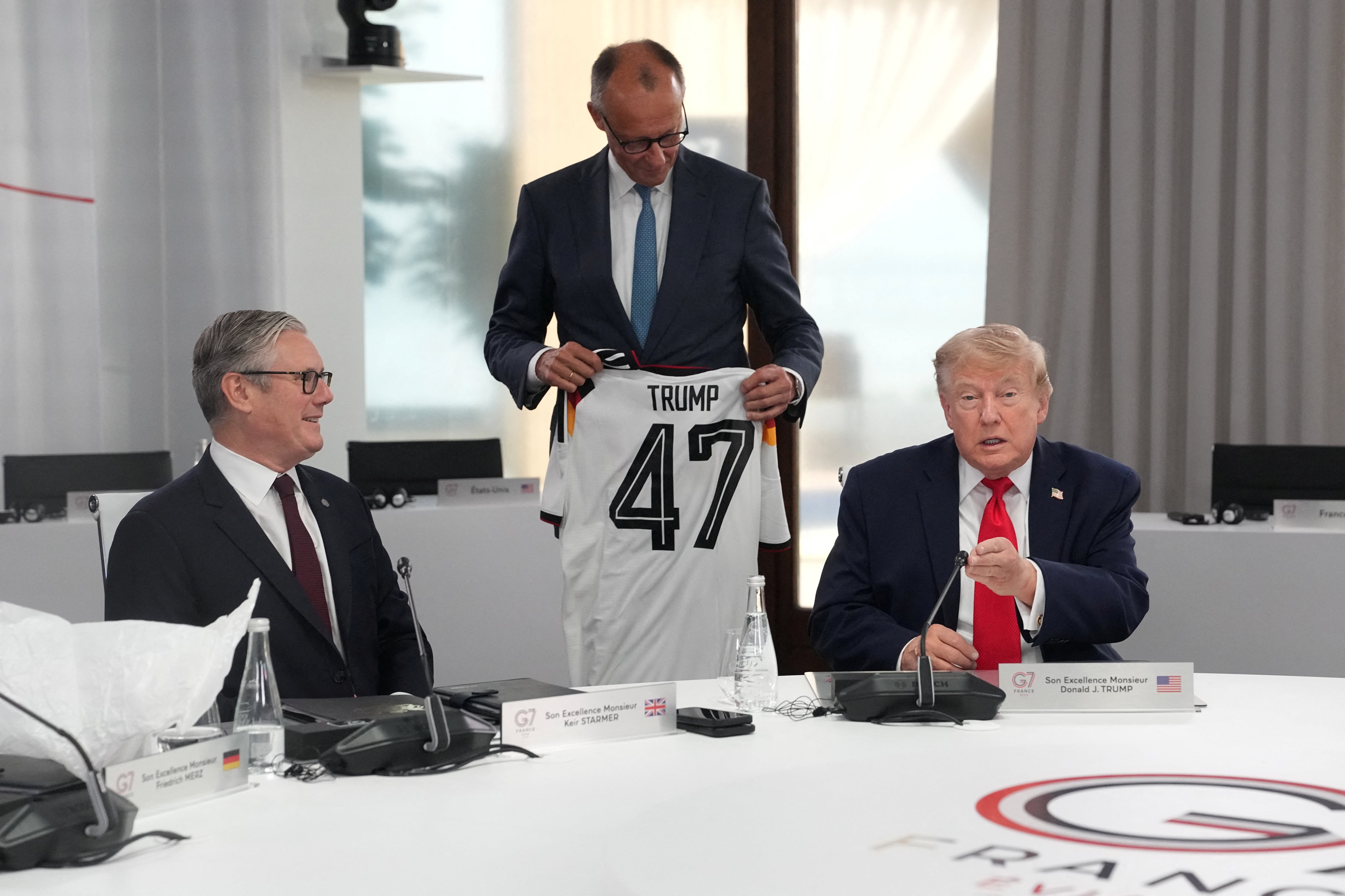 El canciller alemán Friedrich Merz entrega al presidente estadounidense Donald Trump una camiseta con el número 47, mientras el primer ministro británico Keir Starmer observa, durante una sesión de trabajo en la cumbre del G7 en Evian-les-Bains, Francia, el 16 de junio de 2026. Thibault Camus/Pool vía REUTERS