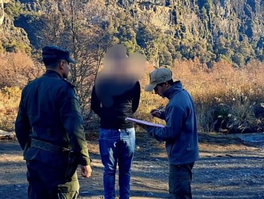 Oficiales del Parque Nacional Nahuel Huapi imponen una multa a turistas brasileños tras infringir regulaciones dentro del área protegida, con un paisaje montañoso de fondo.