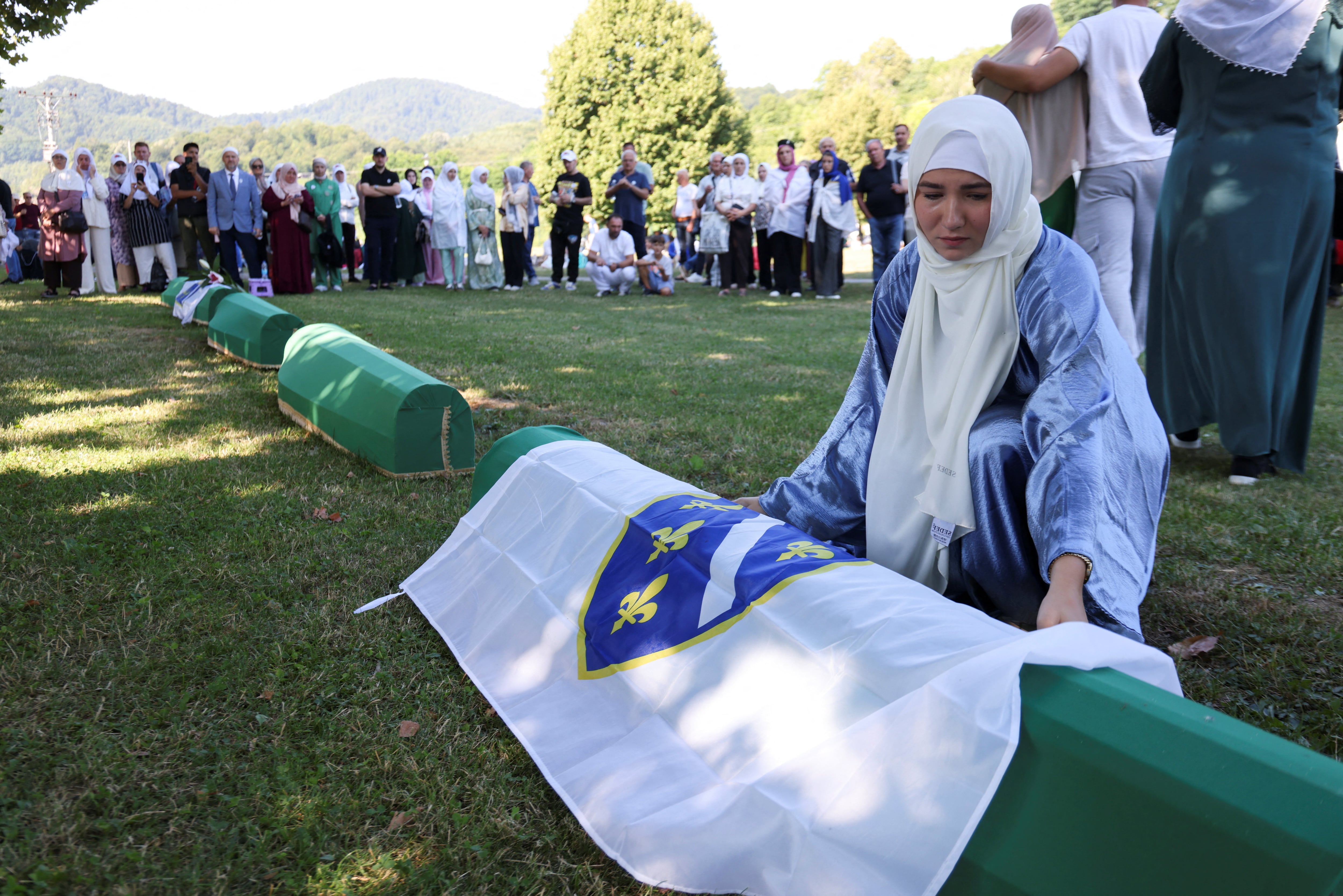 La bosnia Samedina Alihodzic coloca una bandera sobre el ataúd de su padre, Ahmet Guster, una de las diez víctimas cuyo funeral se celebró durante una ceremonia conmemorativa en Potocari, Bosnia y Herzegovina, el 11 de julio de 2026, con motivo del 31.º aniversario del genocidio de Srebrenica. Fotografía: REUTERS/Amel Emric.