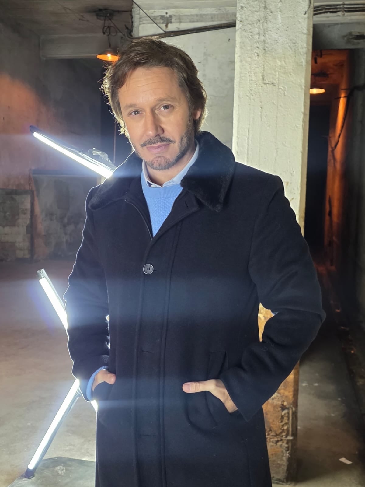 El actor Benjamín Vicuña posa para una sesión de fotos con un abrigo oscuro en un espacio de ambiente industrial.