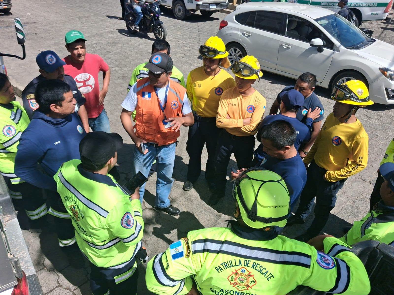 Un grupo de rescatistas y bomberos de Guatemala, identificados por sus uniformes y distintivos, recibe instrucciones en un área al aire libre. (Conred Guatemala)