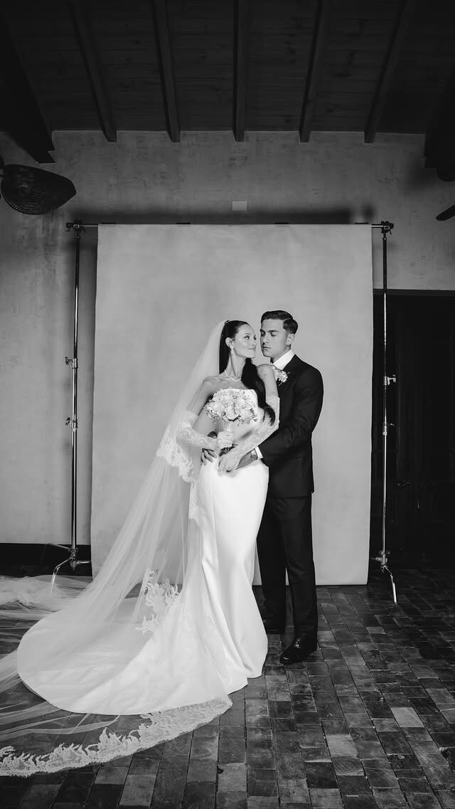 Oriana Sabatini y Paulo Dybala posan abrazados con sus atuendos de boda en un estudio fotográfico con fondo claro.