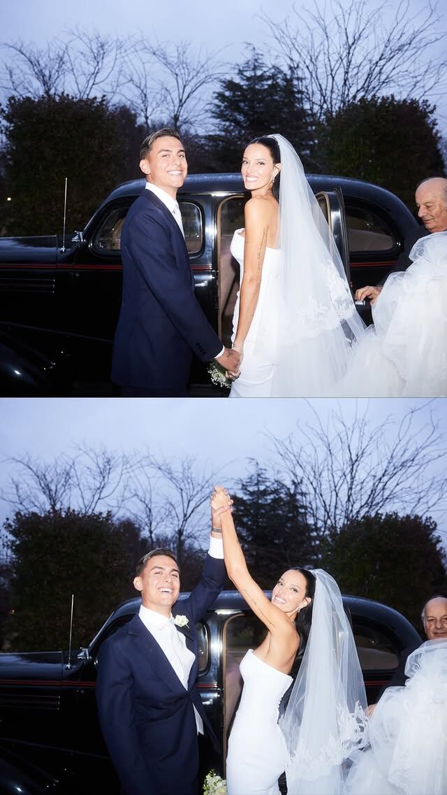 Oriana Sabatini y Paulo Dybala posan sonriendo frente a un auto clásico negro, tomados de la mano y con los brazos en alto, con un hombre mayor detrás, celebrando su segundo aniversario de casados.