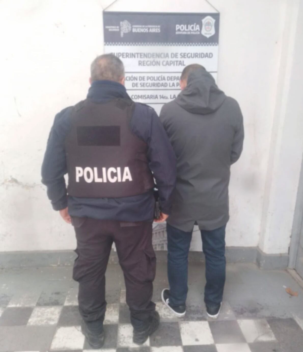 Un agente de la policía de Buenos Aires acompaña a un hombre detenido en una dependencia policial en La Plata tras un allanamiento en el country Grand Bell