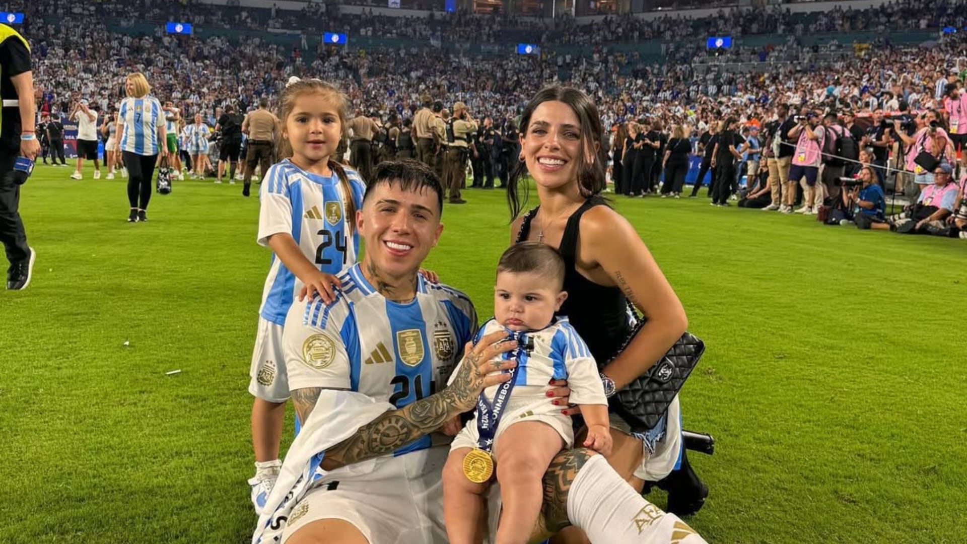 Enzo Fernández posa sonriente junto a su pareja Valentina Cervantes y sus dos hijos en el césped de un estadio, compartiendo un íntimo momento familiar. (Instagram)